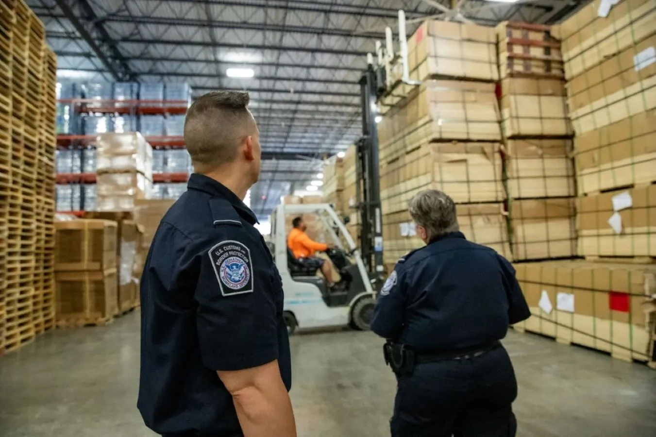Two CBP seized property specialists observe as stacks of seized plywood are stored in a warehouse.